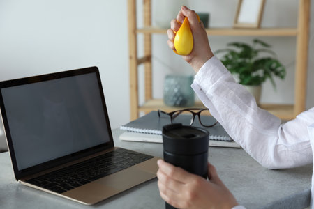 Woman squeezing antistress ball at workplace, closeupの写真素材