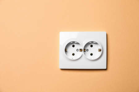 Double power socket on pale orange wall, space for text. electrical supply