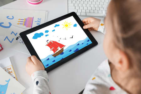 Little girl holding tablet with cute drawing at home. child art