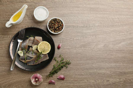 Delicious salted herring fillets served with lemon, thyme and garlic on wooden table, flat lay....