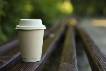 Cardboard takeaway coffee cup with lid on wooden bench outdoors, space for textの写真素材
