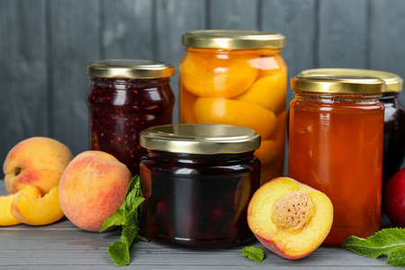 Glass jars with different pickled fruits and jams on gray wooden background