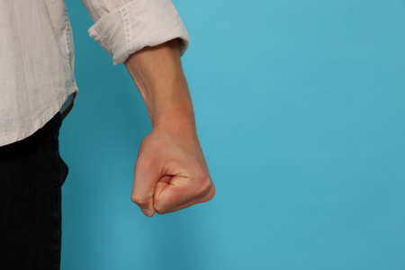Young man showing fist on light blue background, closeup and space for text. Aggression conceptの写真素材