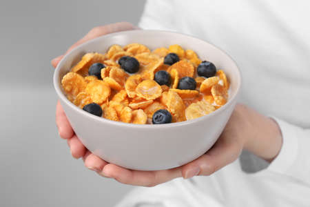 Woman holding bowl of crispy corn flakes with milk and blueberries, closeup