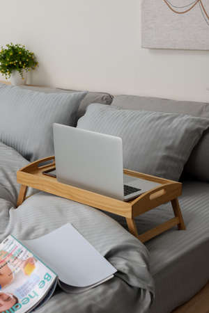 Wooden tray table with laptop and smartphone on bed indoors