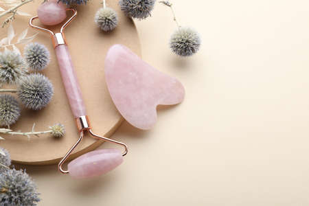Flat lay composition with rose quartz gua sha tool and facial roller on beige background. Space for textの写真素材