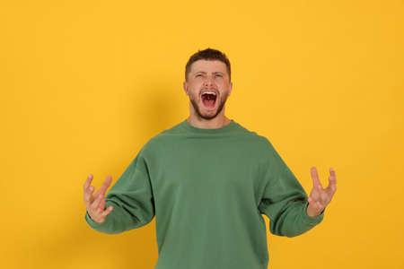 Aggressive young man shouting on orange background