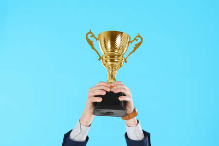 Businessman holding gold trophy cup on light blue background, closeupの写真素材