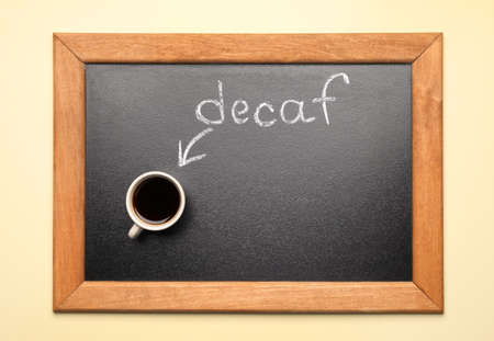 Chalkboard with word decaf and cup of coffee on beige background, top viewの写真素材