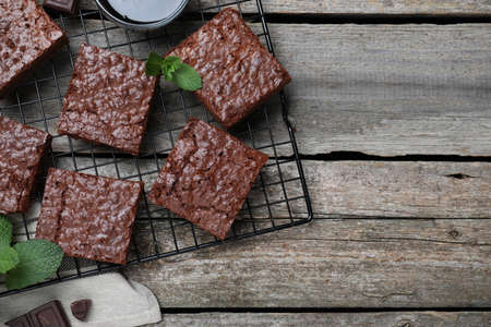 Cooling rack with delicious chocolate brownies and fresh mint on wooden table, flat lay. Space for...