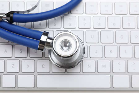 Keyboard and stethoscope on beige background, top view