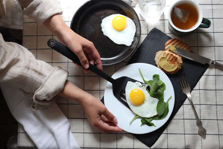 Woman tasty fried eggs onto putting plate at table, top view