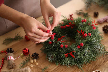 Florist making beautiful Christmas wreath with berries at wooden table indoors, closeupの写真素材