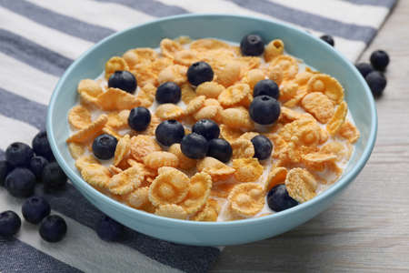 Bowl of tasty crispy corn flakes with milk and blueberries on wooden table, closeup
