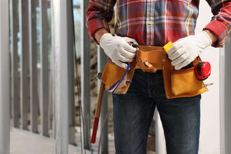 Professional builder with tool belt indoors, closeup