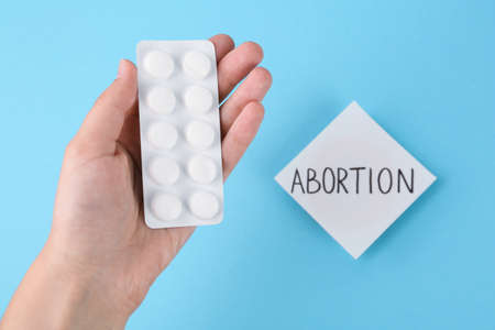 Woman holding pills near paper note with word Abortion on light blue background, top viewの写真素材