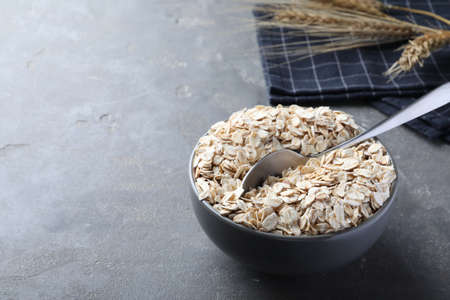 Oatmeal and spoon in bowl on gray table. Space for text