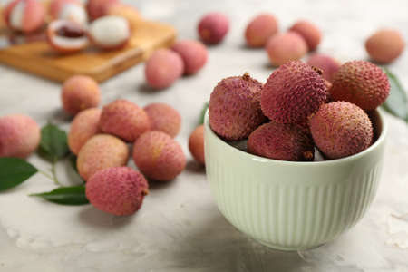 Fresh ripe lychee fruits in bowl on light gray table. Space for text