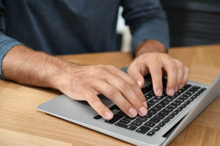 Man using laptop for search at wooden table, closeup