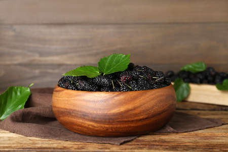 Fresh ripe black mulberries and leaves in bowl on wooden tableの写真素材