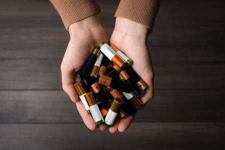 Woman holding many used electric batteries in her hands over wooden table, closeup