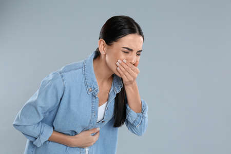 Woman suffering from stomach ache and nausea on gray background, space for text. food poisoning