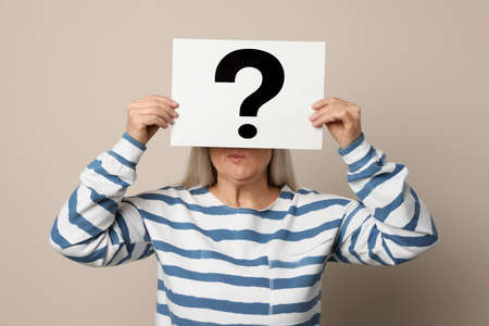 Mature woman holding paper with question mark on beige backgroundの写真素材