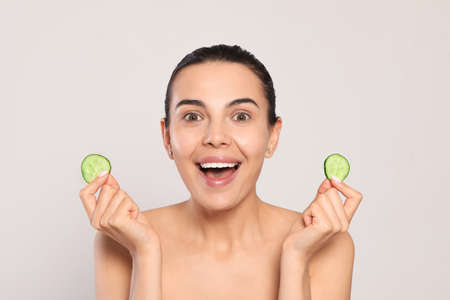 Beautiful young woman with slices of cucumber on light gray backgroundの写真素材