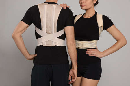 Closeup view of man and woman with orthopedic corsets on gray background