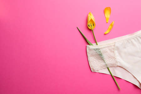 Yellow tulip and panties on pink background, top view with space for text. menopause concept
