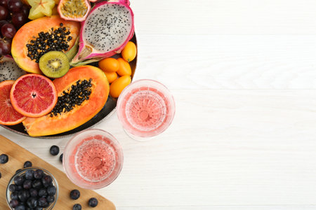 Delicious exotic fruits and wine on white wooden table, flat lay. Space for text