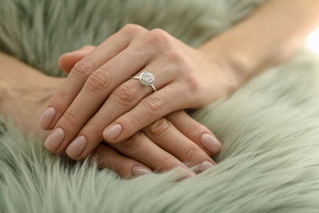 Young woman wearing beautiful engagement ring on faux fur rug, closeupの写真素材