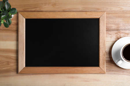 Clean small chalkboard, coffee and plant on wooden table, flat lay