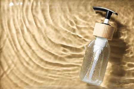 Bottle of cosmetic product in water on beige background, top view. Space for textの写真素材