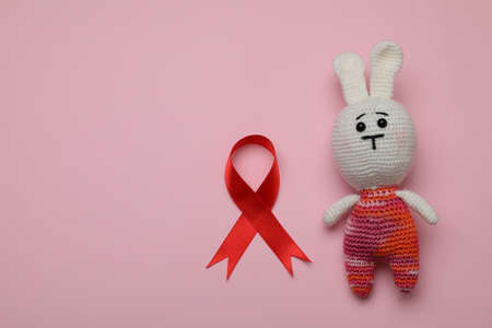 Cute knitted toy bunny and red ribbon on pink background, flat lay with space for text. AIDS disease awarenessの写真素材