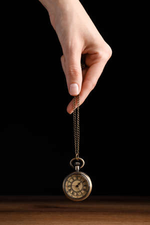 Psychotherapist with pendulum on black background, closeup. Hypnotherapy sessions