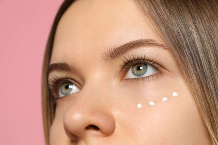 Young woman with cream around eye on pink background, closeupの写真素材
