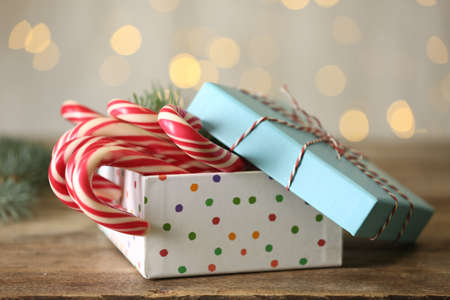 Christmas candy canes in gift box on wooden table against blurred lightsの写真素材