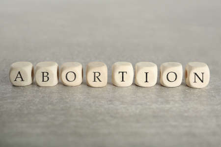 Word Abortion made of wooden cubes on gray table, closeup