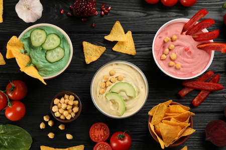 Different kinds of tasty hummus served with nachos on black wooden table, flat layの写真素材