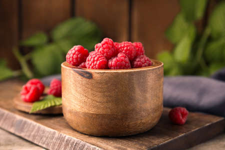 Bowl of fresh ripe raspberries on wooden board, closeup