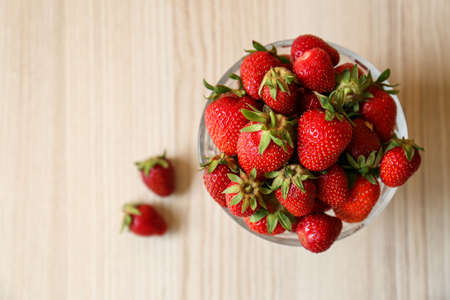 Glass bowl with ripe strawberries on white wooden table, top view. Space for textの写真素材