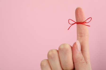 Woman showing index finger with tied red bow as reminder on pink background, closeup, Space for textの写真素材