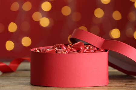Heart shaped chocolate candies in gift box on table against blurred lights. Valentine's day...