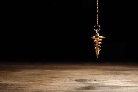Stylish pendulum above wooden table on black background, space for text. Hypnotherapy sessionsの写真素材