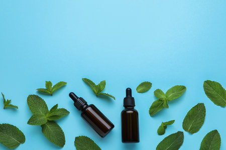 Bottles of essential oil and mint on light blue background, flat lay. Space for text