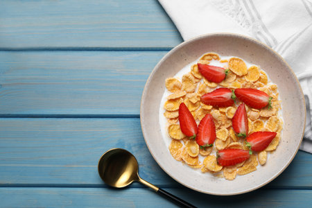 Delicious crispy cornflakes with milk and fresh strawberries on light blue wooden table, flat lay....