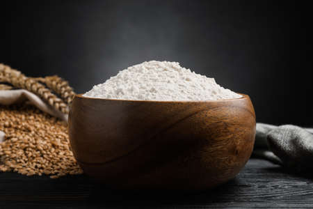 Wheat flour in bowl, spikes and grains on black wooden table, closeupの写真素材