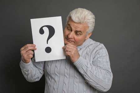 Emotional mature man holding paper with question mark on dark gray background