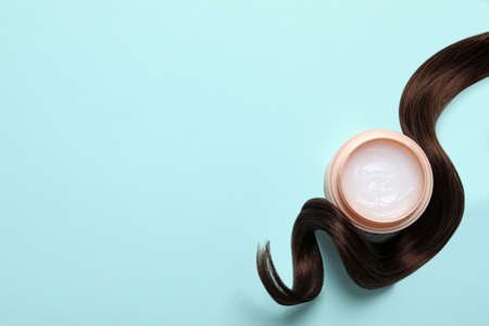 Lock of healthy brown hair and cosmetic product on turquoise background, flat lay. Space for textの写真素材